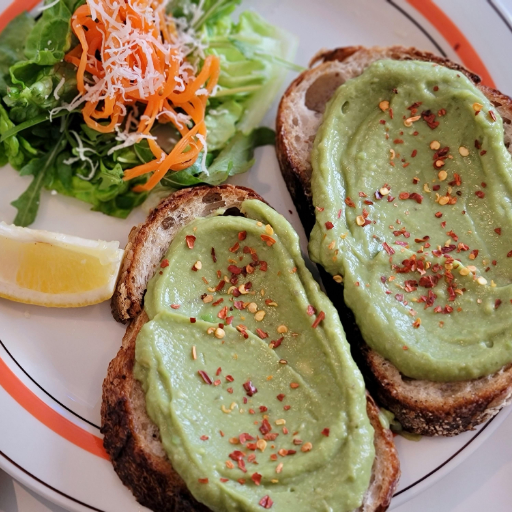 Avocado toast served on a plate with poached egg, chili flakes, and lemon wedge